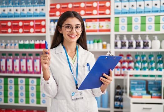 Estudiante con bata y gafas registra medicamentos en farmacia organizada con estanterías surtidas