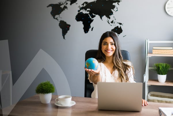 Mujer joven sostiene un globo terráqueo frente a un computador en un espacio de estudio.