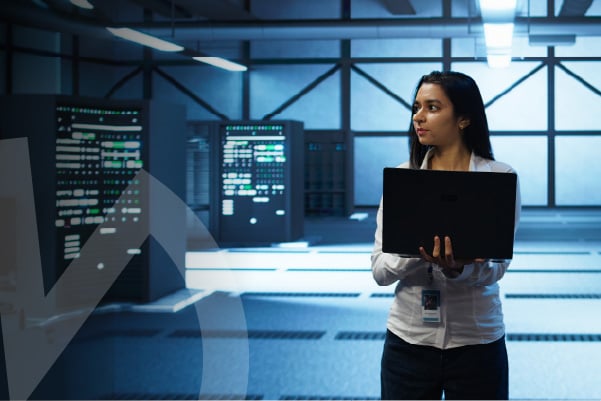 Mujer con computador portátil en un entorno tecnológico con servidores y pantallas digitales.